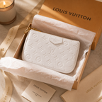 A Louis Vuitton monogram wallet in white textured leather, presented inside its branded kraft gift box with tissue paper, ribbon, dust bag, and a lit candle on a warm neutral surface.