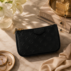 A black embossed Louis Vuitton zip pouch with gold-tone hardware, styled on a marble surface with books, jewelry, and flowers.