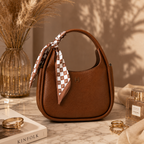 A brown pebbled leather hobo handbag with a top handle, decorated with a brown and white checkered silk scarf tied around the handle. The bag features a small gold 'H' logo on the front.