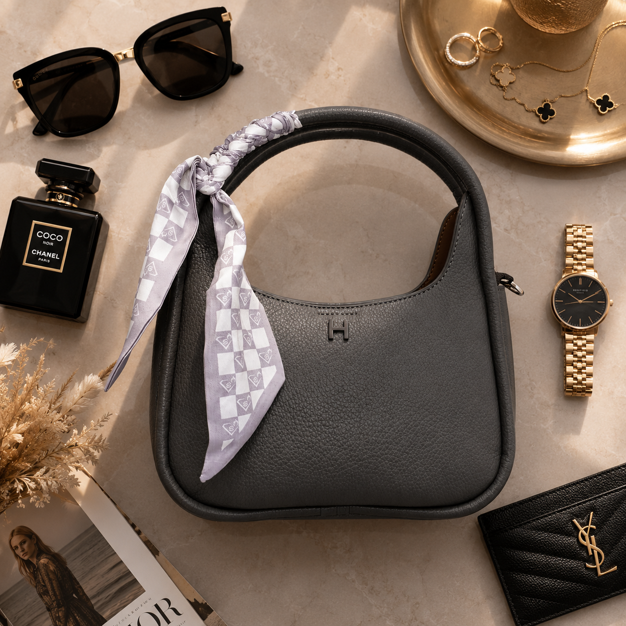 A dark gray pebbled leather shoulder bag with a structured top handle, decorated with a light purple and white checkered scarf. The bag features a small embossed 'H' logo on the front.