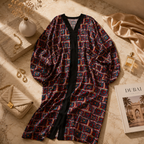 A long open-front robe with a multicolor geometric pattern and black trim, styled on a marble surface with a quilted handbag, perfume bottle, dried flowers, and a magazine.