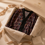 A luxury gift set from Dubai Jewelry Collection featuring a patterned robe in a beige box lined with tissue paper and ribbon, accompanied by a branded card.