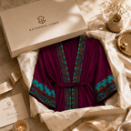 A luxury robe from External Links, presented in a cream-colored gift box with branded packaging, surrounded by elegant props like dried flowers, a gold candle holder, and a small gold dish on a beige marble surface.