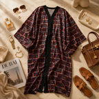 A patterned open-front kaftan robe with a black center placket and wide sleeves, styled in a luxury flat lay with sunglasses, perfume, jewelry, a handbag, sandals, and a Dubai magazine on a beige marble surface.