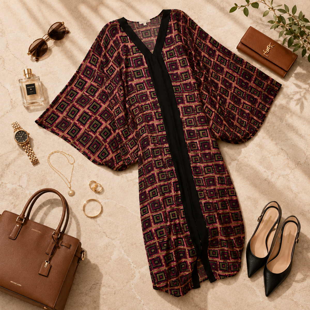 A patterned open-front kimono-style cardigan with wide sleeves is styled in a flat lay on a beige marble surface with sunglasses, a perfume bottle, a watch, jewelry, a brown handbag, a brown YSL clutch, and black pointed heels around it.