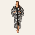 A woman modeling a long black and white zebra-print kaftan robe with a black inner dress, standing against a solid white background.