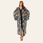 A woman modeling a long black and white zebra-print kaftan robe with a black inner dress, standing against a solid white background.
