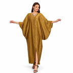 A woman modeling a flowing, floor-length caftan dress in a shimmering mustard gold color, featuring wide draped sleeves, a V-neckline, and a front slit, set against a plain white background.