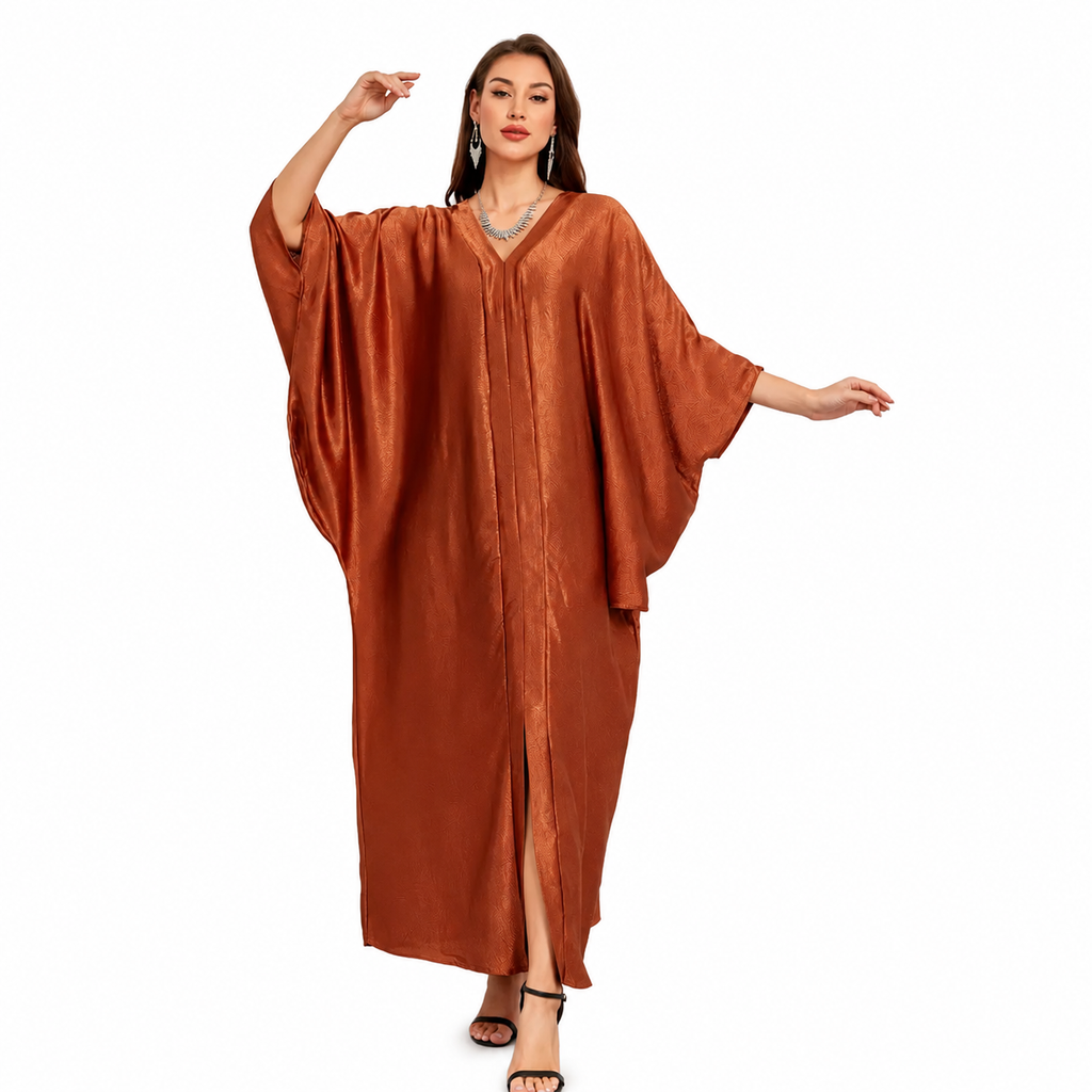 A woman modeling a flowing, rust-brown kaftan dress with wide draped sleeves and a front slit, set against a plain white background.