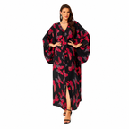 A woman modeling a long black kaftan dress with a red and pink abstract floral pattern, featuring wide balloon sleeves, a V-neckline, and a front slit, set against a plain white background.