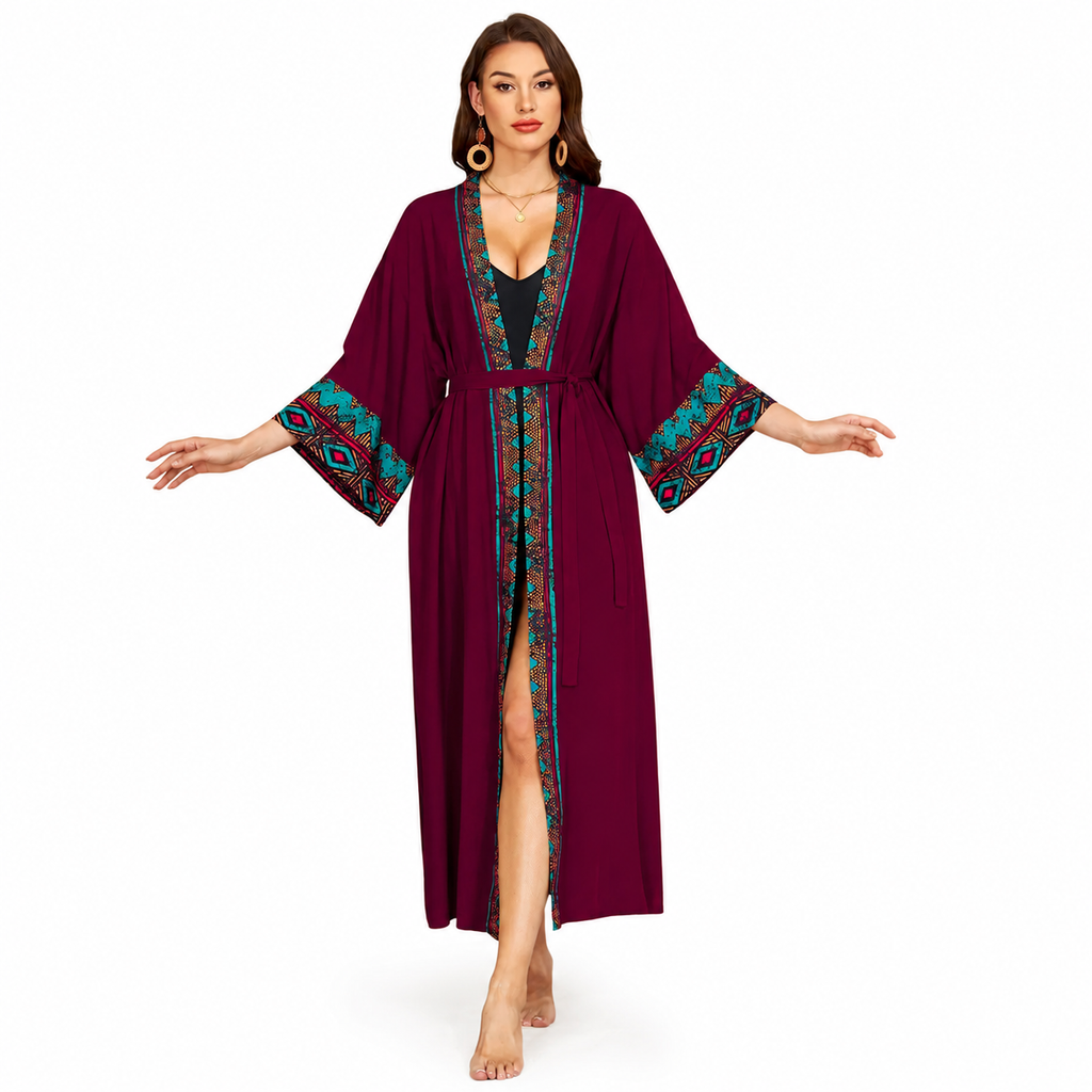 A woman modeling a long burgundy kimono-style robe with teal, red, and gold patterned trim on the collar, front opening, and wide sleeves, shown against a plain white background.