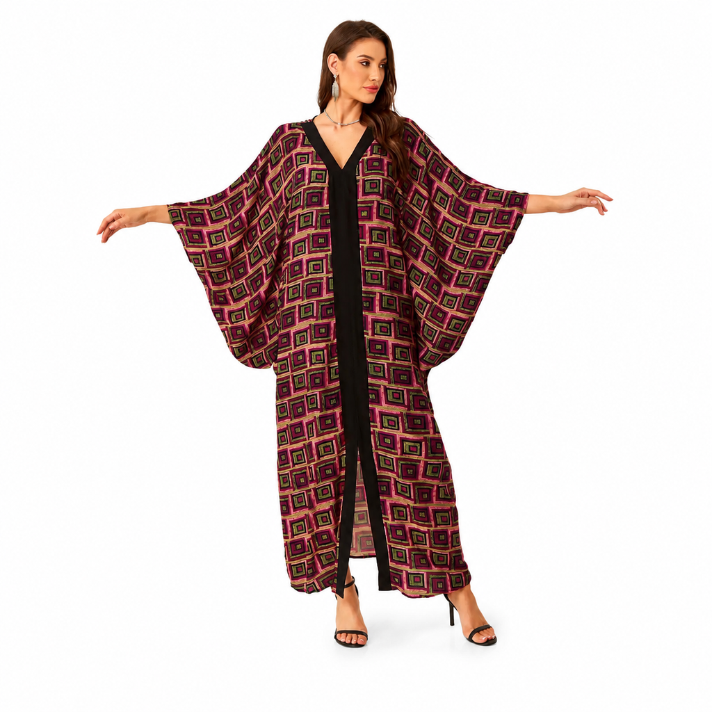 A woman modeling a long, flowy kaftan-style cover-up with wide sleeves and a geometric print in dark red, black, and gold, worn over a black jumpsuit against a plain white background.
