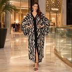 A woman models a long black and white zebra-print robe with a black center panel and front slit, standing in a luxury shopping mall corridor with Valentino storefronts in the background.