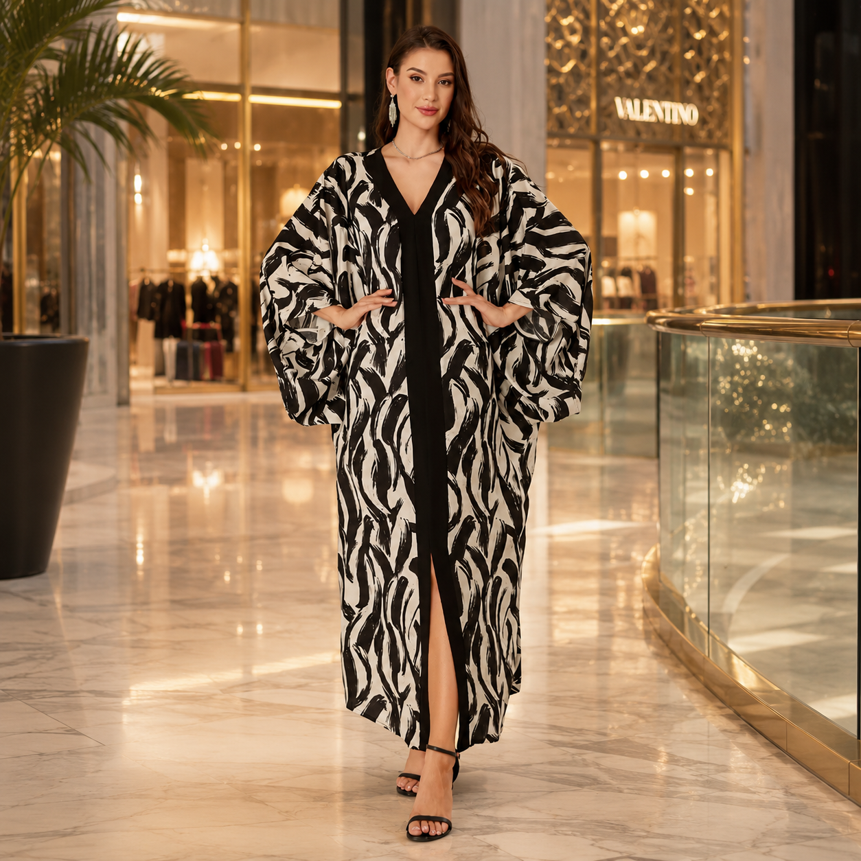 A woman models a long black and white zebra-print robe with a black center panel and front slit, standing in a luxury shopping mall corridor with Valentino storefronts in the background.