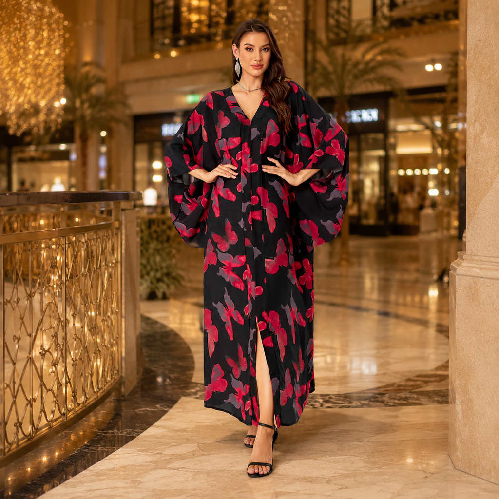 A woman models a long black maxi dress with a vibrant red and pink abstract floral pattern, standing in a luxurious indoor lobby with warm lighting.