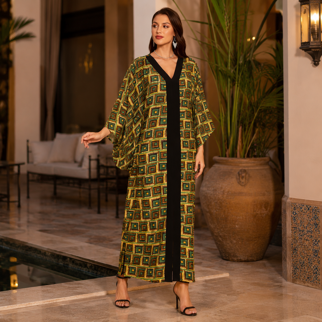 A woman models a long, loose kaftan dress with a green and yellow geometric pattern and a black V-neckline, set in an elegant indoor courtyard with a pool and potted plants.