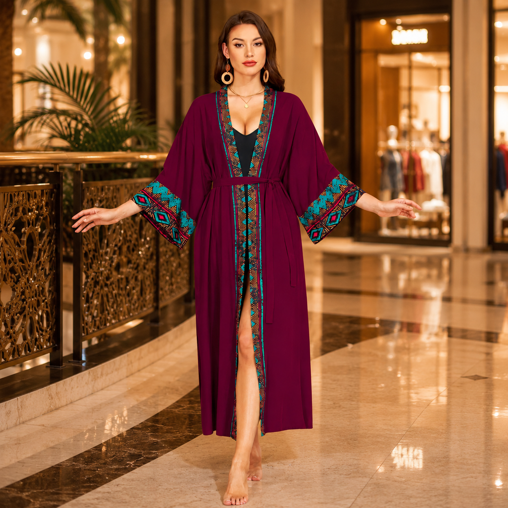 A woman stands barefoot in a luxury shopping mall corridor wearing a long, deep purple kaftan robe with teal and gold patterned trim on the sleeves, collar, and front opening.