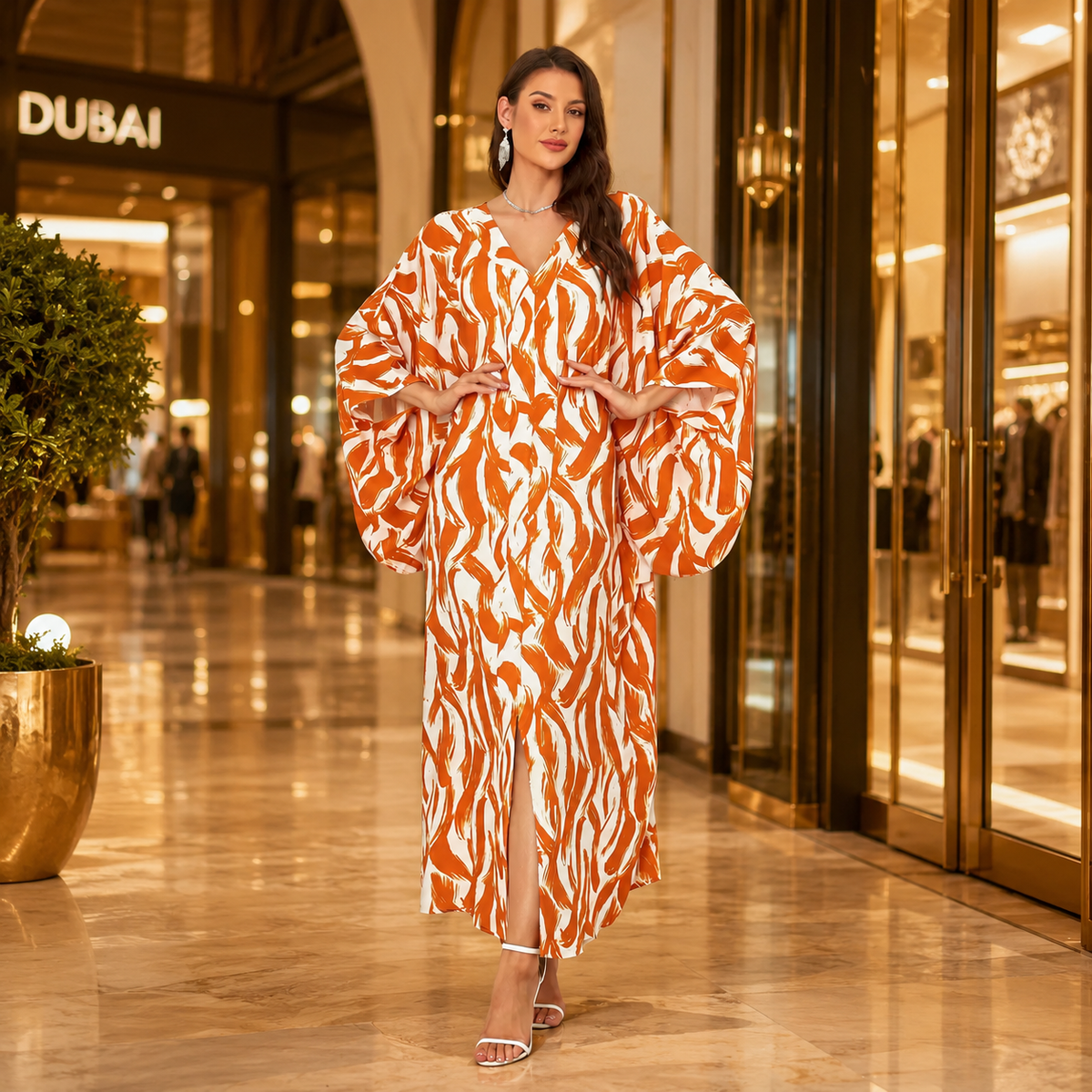 A woman stands in a luxury shopping mall corridor wearing a long, flowing caftan-style dress with a bold orange and white abstract pattern. The background features a Dubai store entrance and polished marble floors.