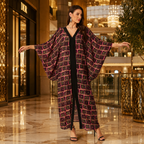 A woman stands in a luxury shopping mall wearing a long, wide-sleeved black dress with a magenta and gold geometric patterned overlay. The background features a Dior storefront and elegant interior details.