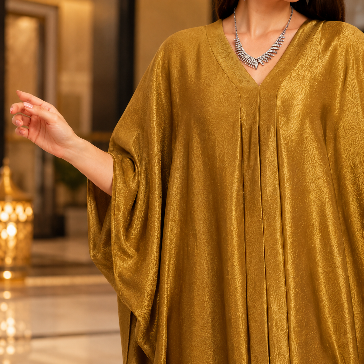A woman wearing a loose, flowing kaftan dress in a rich mustard-gold color with a subtle woven pattern. The dress features a V-neckline and wide draped sleeves.