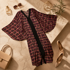 A women's open-front kimono-style cover-up with wide bell sleeves, laid flat on a marble surface. The garment has an allover geometric pattern in dark purple, pink, and black, with a solid black center panel and trim.
