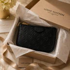 A black Louis Vuitton monogram zip pouch resting in an open branded box lined with tissue paper, with the Louis Vuitton box lid and ribbon visible around it.