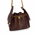 A dark brown quilted leather handbag with gold-tone hardware, featuring a drawstring top, a front flap pocket with a gold CC turn-lock, and a gold chain strap, shown on a white background.