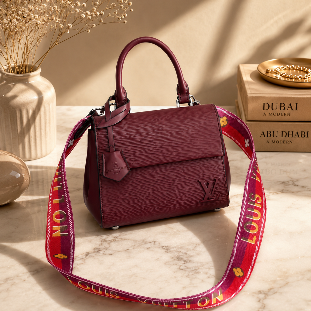 Luxury burgundy handbag displayed on marble surface with soft beige tones and sophisticated editorial fashion accessories.