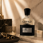 Creed Aventus perfume styled on marble surface with luxury accessories and soft beige tones.