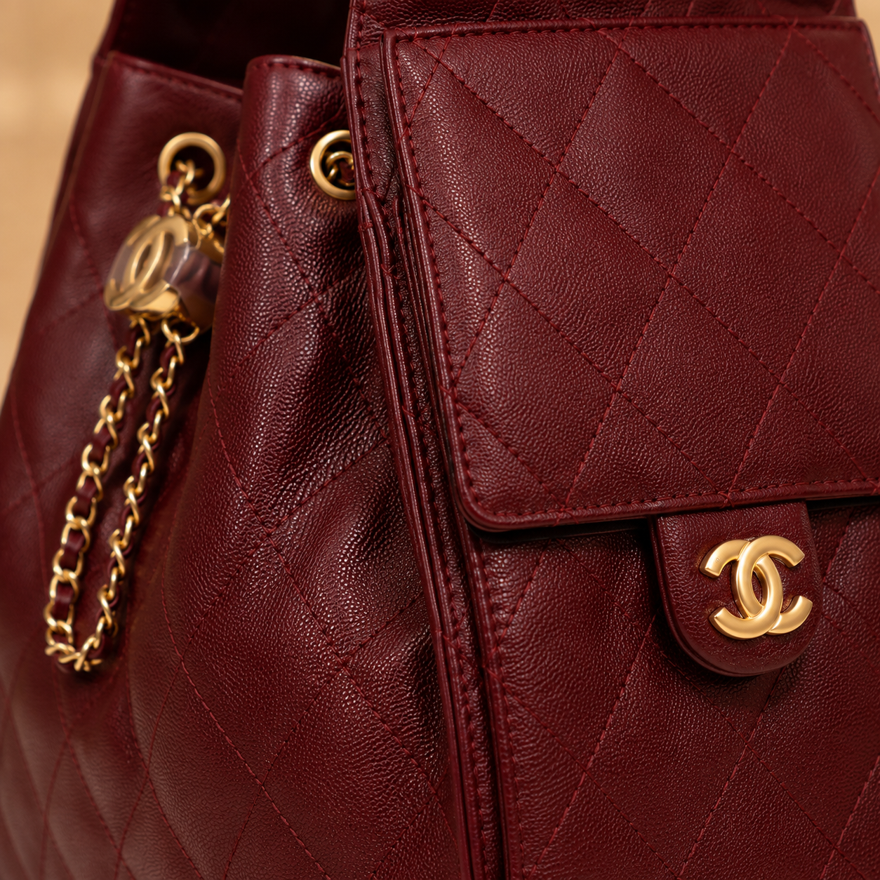 Close-up of a quilted burgundy leather handbag with gold-tone hardware, featuring a flap pocket with a Chanel CC turn-lock and a hanging chain charm.