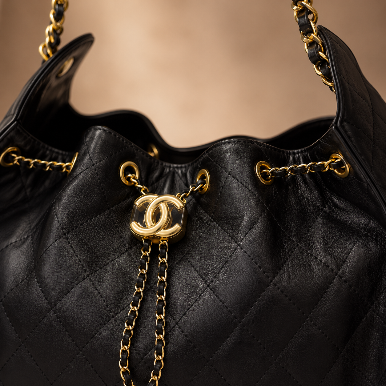 Close-up of a black quilted leather handbag with gold-tone chain straps and a prominent interlocking CC logo clasp, showing the texture and details of the bag against a warm beige background.