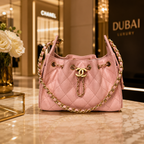 A pink quilted leather shoulder bag with gold-tone hardware and a chain strap, displayed on a marble surface in a luxury retail setting. The bag features the interlocking CC logo on the front.