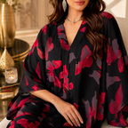 A woman wearing a black kaftan-style robe with a bold red and dark purple floral print, styled in a warm, elegant indoor setting.
