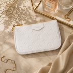A white embossed Louis Vuitton zip pouch with gold-tone hardware, styled on a beige marble surface with dried flowers, a Chanel perfume bottle, and gold jewelry.